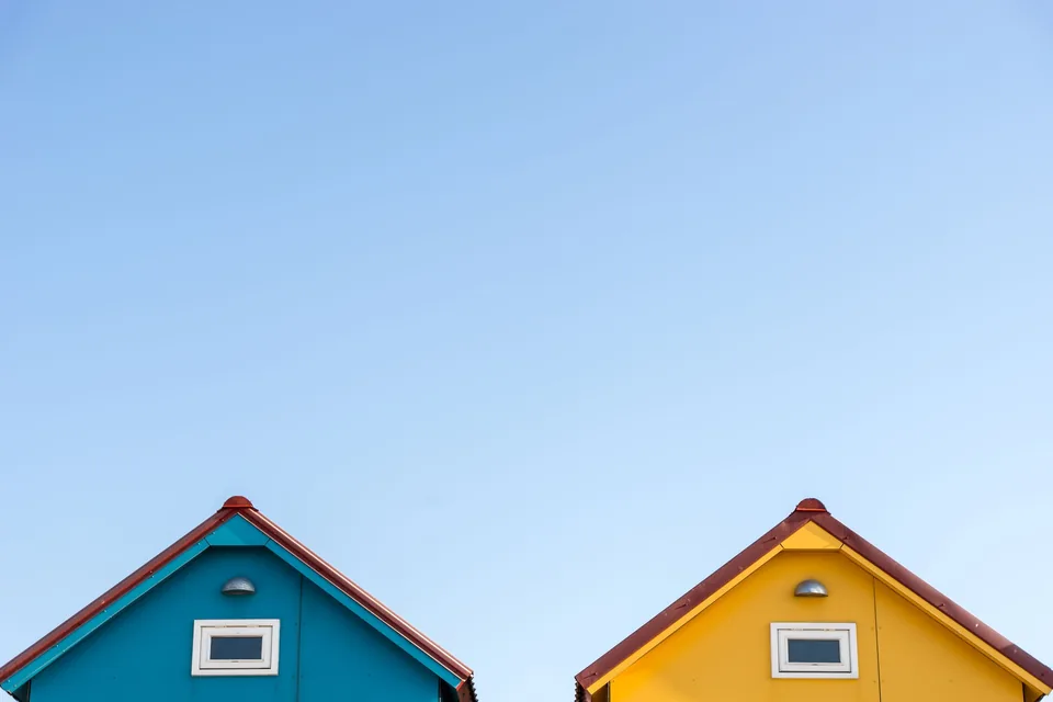 Two small gabled houses side by side, blue and yellow, under a clear sky
